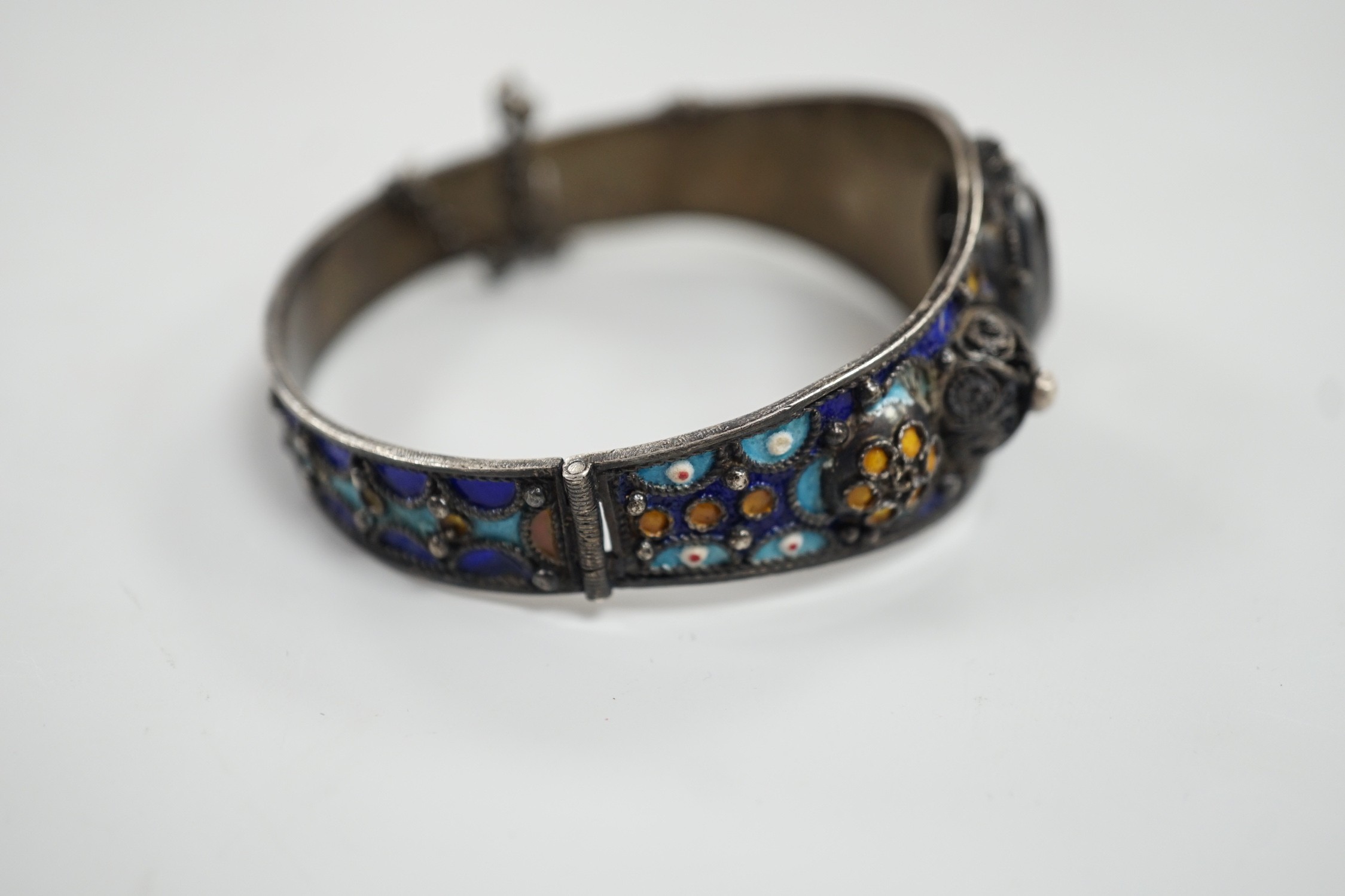 An early to mid 20th century continental white metal polychrome enamel and foil backed oval cut rock crystal set hinged bangle, interior diameter approximately 62mm.